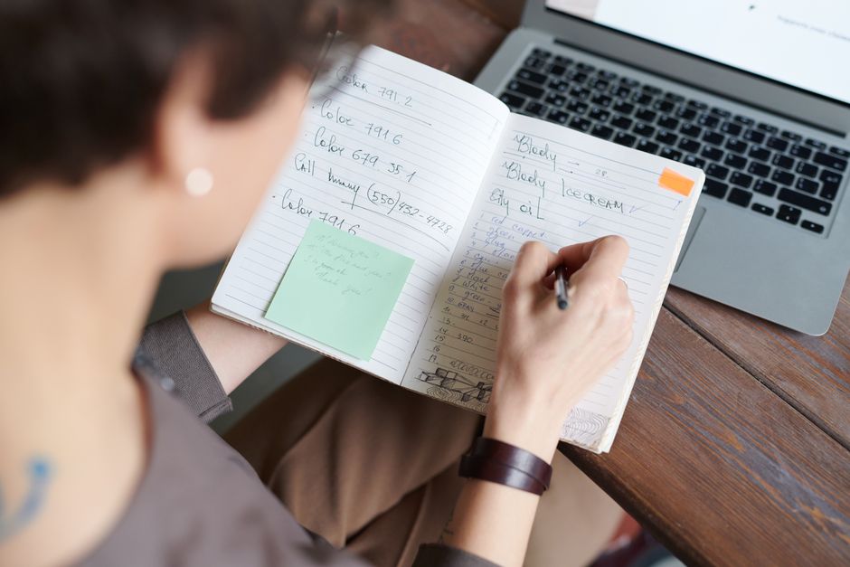 person writing notes at laptop