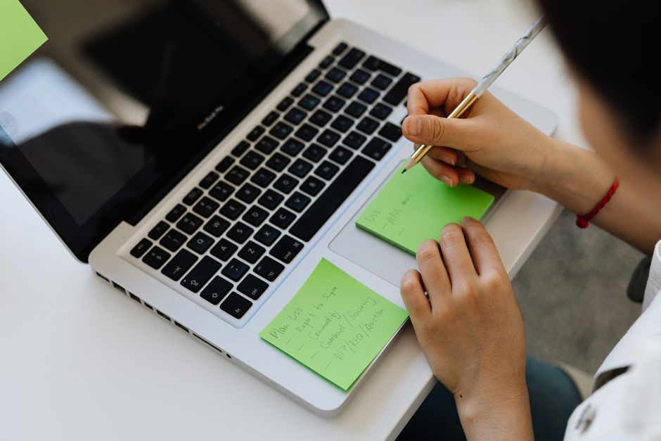 person writing notes at laptop desk