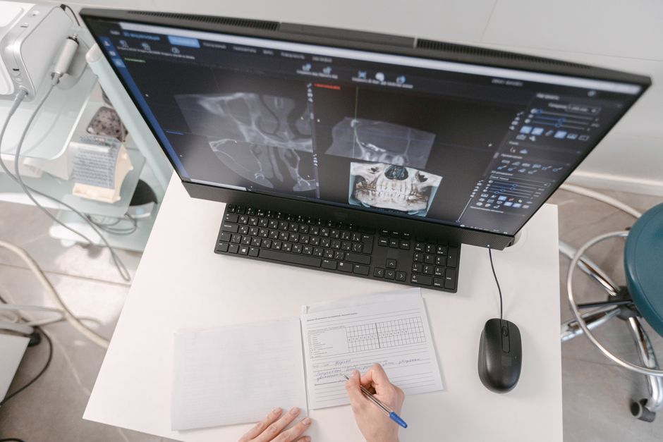 hands writing notes at desk with monitor