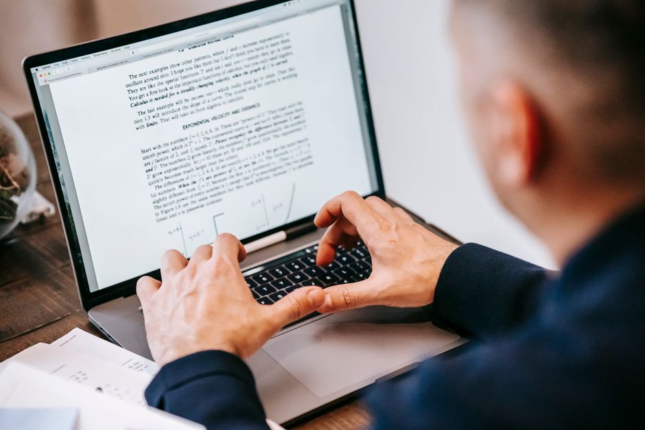 person typing at laptop with documents